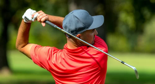 Golfer in red polo and a hat on that just finished a swing